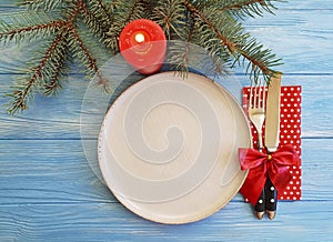 Plate, fork, knife, serving setting dish festive decor of a Christmas tree, candle on a blue wooden background