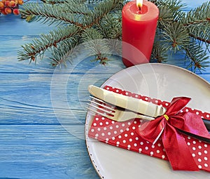 Plate, fork, knife, serving setting festive decor of a Christmas tree, candle on a blue wooden background