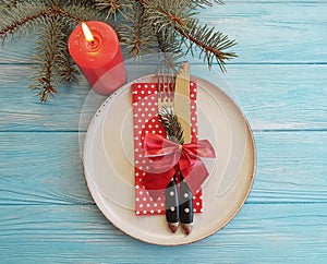 Plate, fork, knife, serving setting festive decor seasonal of a Christmas tree, candle on a blue wooden background