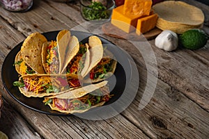 Plate with fragrant mexican tacos on rustic wooden table with ingredients for cooking background. Concept of traditional meal.