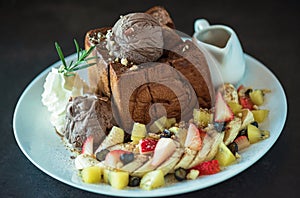 Plate of french toast topped with chocolate ice cream, mixed berries, banana and maple syrup and on dark background