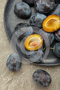 A plate of fresh blue plums on grey concrete background. Vertical photo