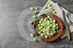 Plate of fresh Brussels sprouts, napkin and knife on grey background