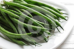 Plate with fresh green French beans on table