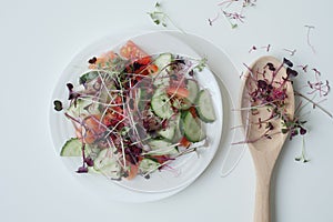 Plate with fresh salad and microgreens with a wooden spoon on a white table. Healthy food, superfood