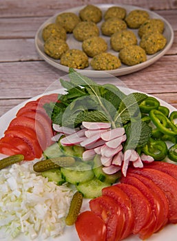Plate of fresh vegetable salad, tomato, cucumber, onion, gherkin, radish, mint leaves and falafel