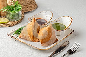 Plate of freshly-fried samosas accompanied by two dipping sauces