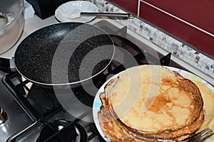 Plate of freshly made crepes and frying pan on stove in kitchen