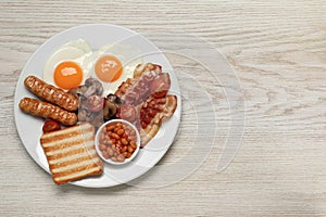 Plate of fried eggs, sausages, mushrooms, beans, bacon and toast on white wooden table, top view with space for text. Traditional