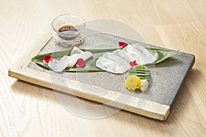 Plate of fugu sashimi garnished with edible flowers on wooden background