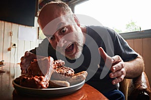 A plate full of barbecues and a man looking very excited to eat it and his mouse open