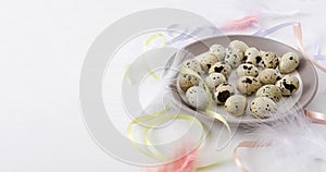 Plate full of quail eggs, colorful ribbons and birds feathers on the white table.Empty space for greeting