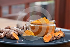 Plate with glass jar of turmeric powder and fresh roots on table