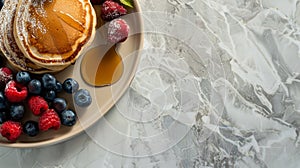 A plate of golden pancakes topped with syrup and surrounded by fresh berries, set against a marbled white background