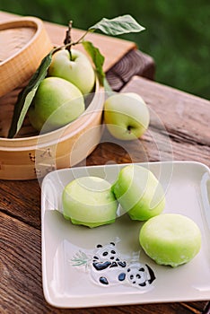 A plate of green apples and a basket of apples on a wooden table. Mochi asian dessert