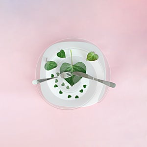 Plate with green leaves hearts and silverware. Valentine design aesthetic on a pink background.Love abstract