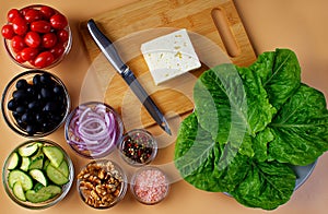 A plate with green salad leaves and a cutting board with feta cheese and a knife next to it. Seven bowls with tomatoes, black