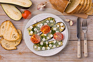 Plate of grilled eggplant with feta cheese and grilled tomatoes on a white wooden background, top view