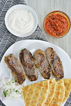 Plate with grilled kebabs ,pita bread and chopped onion and yogurt and tomato sauce in bowls