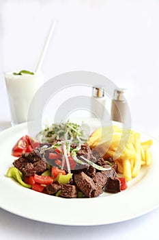 A plate with grilled liver, onion, vegetables, potatoes and ayran