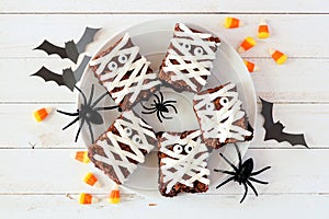 Plate of Halloween mummy brownies, top view with decor on white wood