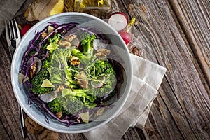 Plate with a healthy vegetarian salad of steamed broccoli, fresh radishes, walnuts, red cabbage, ginger and extra virgin olive oil photo