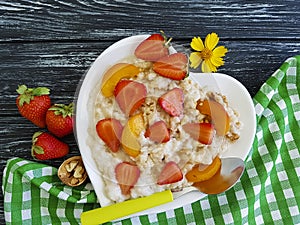 Plate heart oatmeal porridge, fresh strawberry, apricot on a wooden background