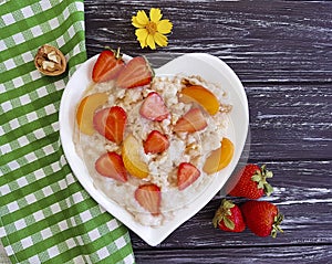 Plate heart oatmeal porridge, fresh summer strawberry, apricot on a wooden background