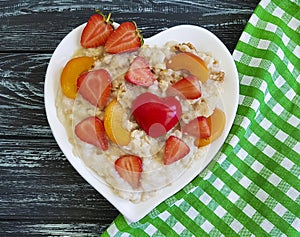 Plate of heart oatmeal porridge, strawberry, apricot on a wooden background