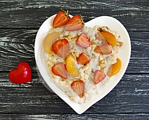 Plate heart oatmeal porridge, strawberry, apricot on a wooden background