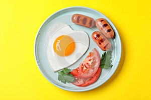 Plate of heart shaped fried egg and sausages on yellow, top view