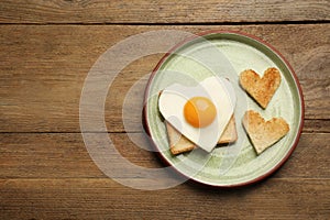 Plate with heart shaped fried egg and toasts on wooden table, top view. Space for text