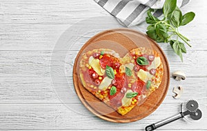 Plate with heart-shaped pizza, ingredients and knife on wooden background