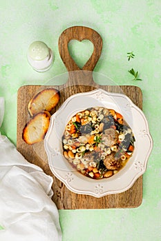 A plate of homemade Minestrone soup with meatballs and spinach on a green background.