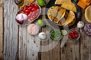 Plate with hot mexican tacos on rustic wooden table with ingredients for cooking background. Concept of traditional meal.