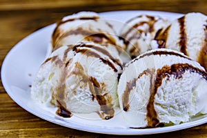 Plate with ice cream balls and chocolate topping on a wooden table