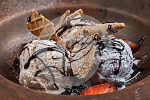 Plate with ice cream and waffles, poured with chocolate topping and decorated with strawberries.