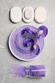 Plate and jar with purple sea salt, spa stones, beautiful flower on grey marble table, flat lay