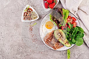 Plate with a keto diet food. Fried egg, bacon, avocado, arugula and strawberries.