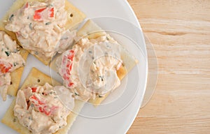 Plate of lobster dip on saltine crackers atop wood table