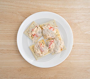 Plate of lobster dip on saltine crackers atop wood table