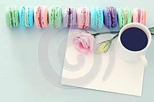 plate of macaroons over wooden table cofee, empty note and flowers.
