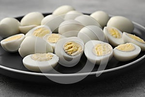 Plate with many peeled hard boiled quail eggs on grey table