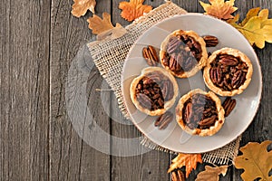 Plate of pecan pie tarts, overhead table scene on wood