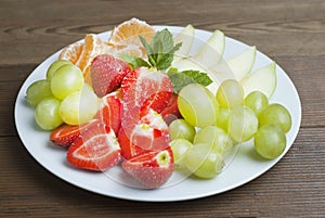 A plate with mixed fruits and sliced fruits. Delicious snack for kids or adult. Strawberries, apple, tangerine citrus and grape. V