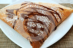 Plate of Mouthwatering French Crepe with Chocolate Sauce and Icing Sugar photo