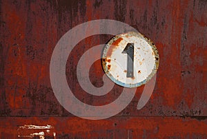 The plate with the number 1 on a rusty metal wall.