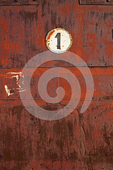 The plate with the number 1 on a rusty metal wall.