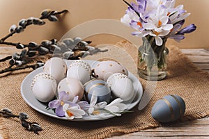 Plate with painted Easter eggs, spring flowers and willow branches on a wooden table. Easter greeting card. Closeup