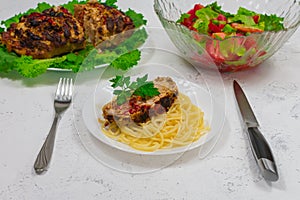 A plate of pasta and a large piece of pork cooked in the oven, baked in the oven. Oven baked meat on green lettuce